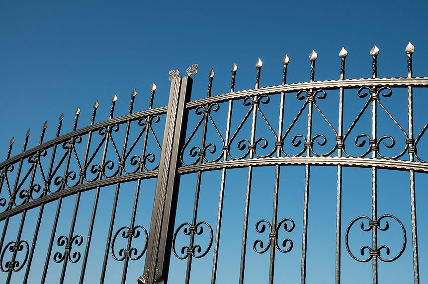 Ornate wrought iron gate with scrollwork and spear-point finials against blue sky