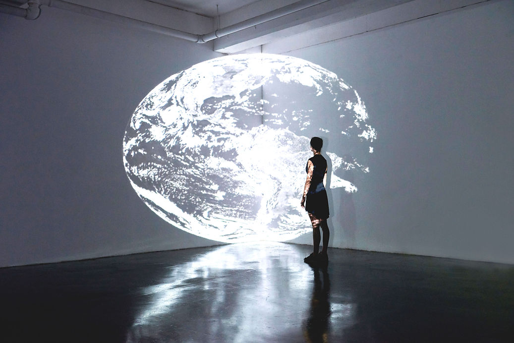 A female appearing persin standing in front of a projected image of the Earth on a wall.