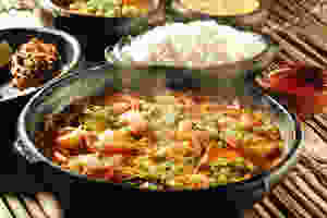 Cardápio de pratos variados de comida servidos em panelas de barro sobre uma mesa rústica