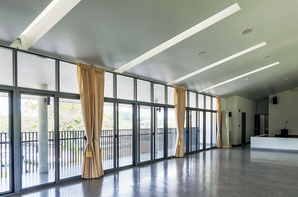 Spacious multi-purpose hall with floor-to-ceiling glass sliding doors, beige curtains, and polished reflective floor.