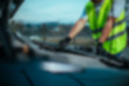A mechanic in a reflective vest checks the engine of a car