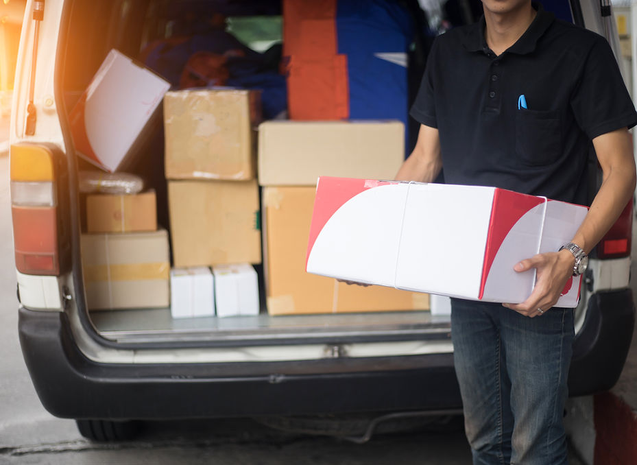 Close-up of a person carrying a white and red parcel from the back of a loaded delivery van