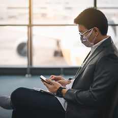 Man wearing mask using phone near window and airplane at airport