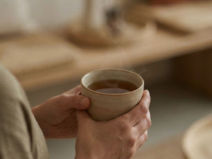 Close-up of a person seated indoors, holding a mug with both hands in soft natural light.