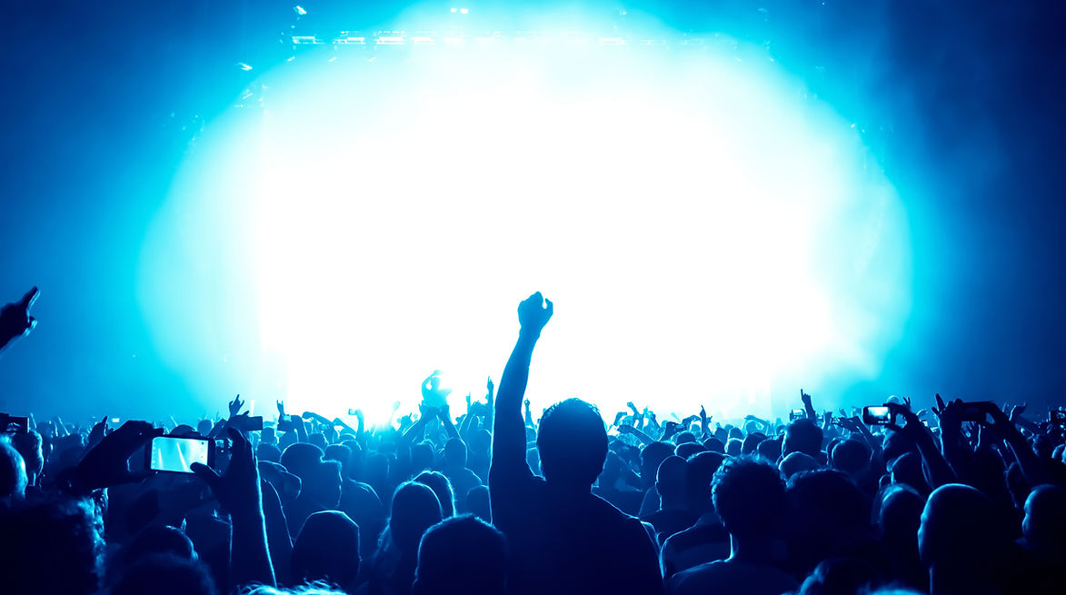A lively crowd at a concert silhouetted against bright blue and white lights