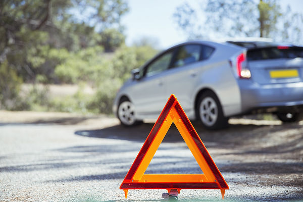Red emergency warning triangle positioned behind a broken down car awaiting roadside breakdown recovery