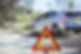 A bright orange warning triangle stands in front of a silver car parked