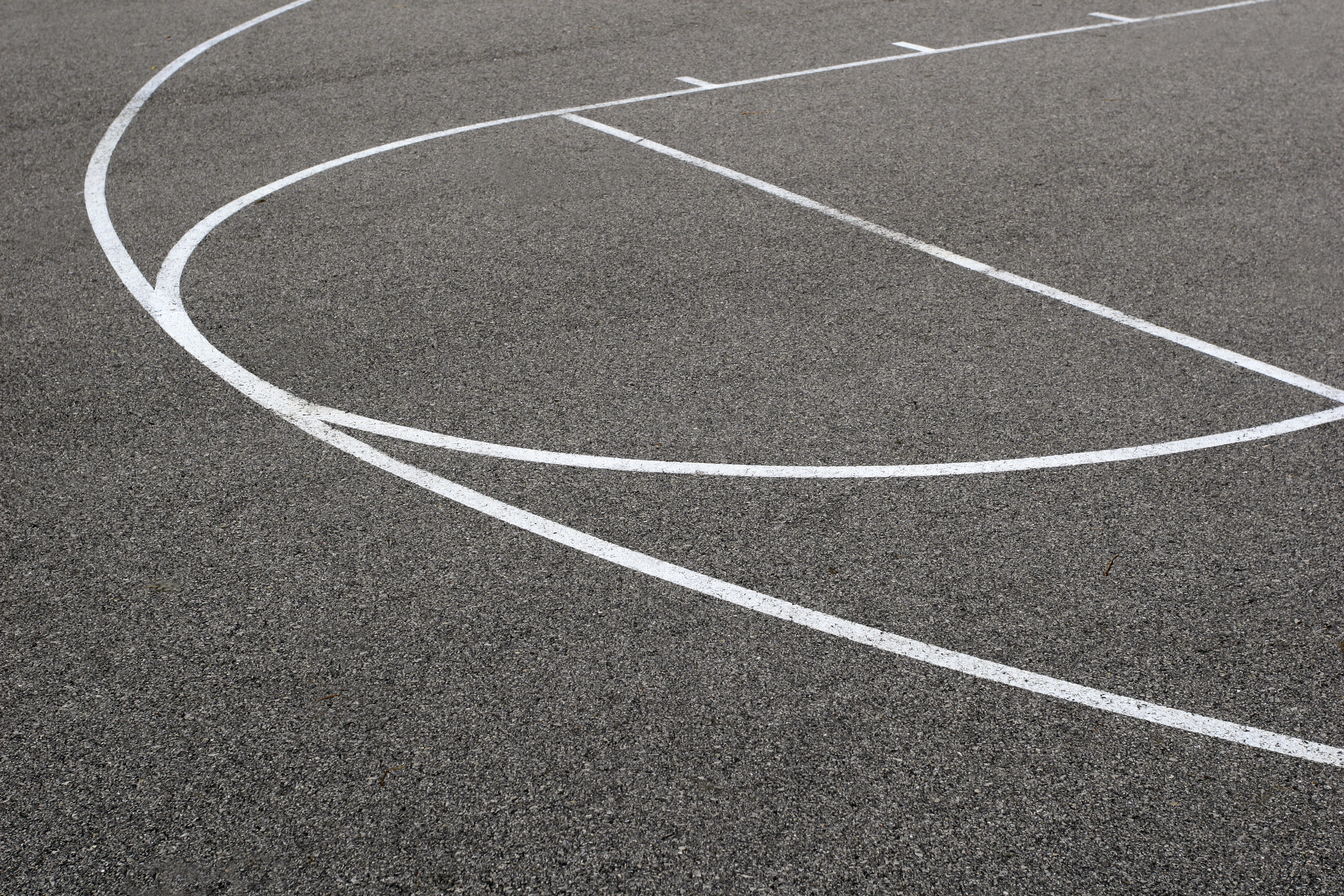 Crisp curved white sports court line freshly painted on a dark textured tarmac surface