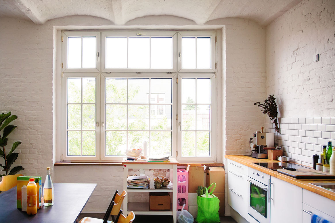 Window into sunny white European kitchen. Fresh groceries are in bags on the floor