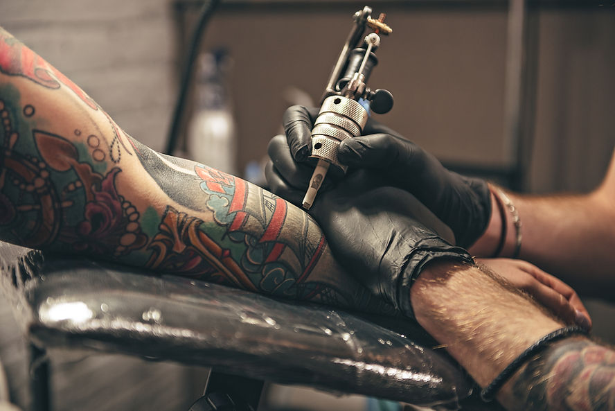 A tattoo artist wearing black gloves works on a colorful tattoo sleeve on a person's arm