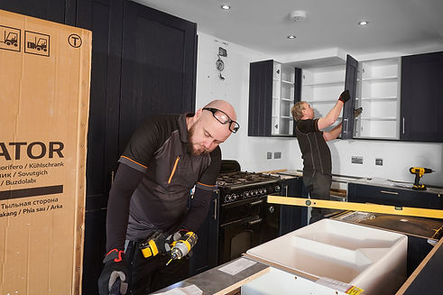 Tradespeople fitting kitchen wall cabinets and working with power tools during residential kitchen refurbishment UK