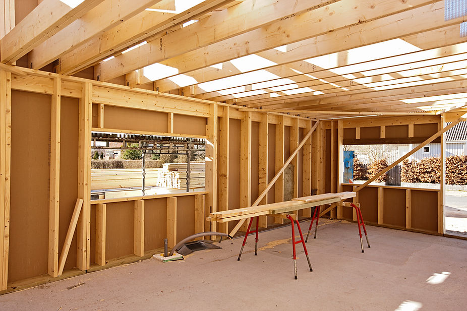 A house construction site showing a raw wooden wall frame setup with outdoor scaffolding visible through a cutout window