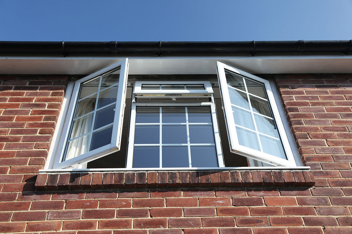 An open, double-pane window in a brick wall against a clear blue sky