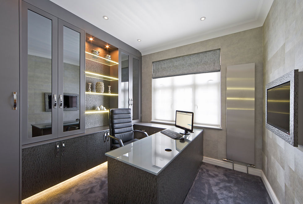 a modern, bespoke home office featuring dark grey fitted cabinetry, built-in illuminated shelving, and a matching desk with a glass top