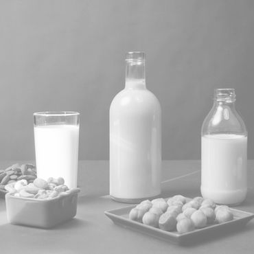 Bottles and glasses of milk on a table with bowls of almonds and nuts. Neutral grey background. Simple and calm composition.