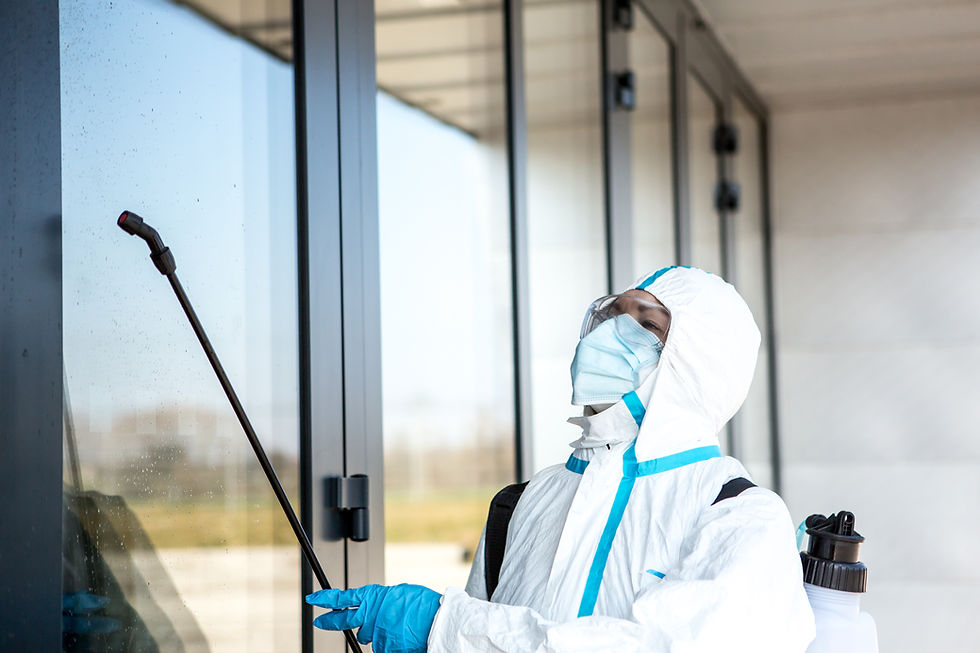 Worker in PPE suit spraying disinfectant on glass door