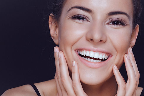 A close-up beauty portrait of a beautiful, smiling young woman gently holding her clean, n