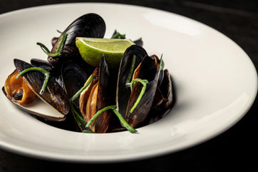 Cooked mussels with lime and greens in a white dish.