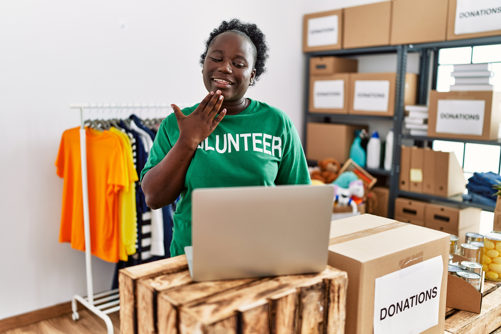 Woman with a green t-shirt with the word volunteer in from of a computer in a warehouse with clothes