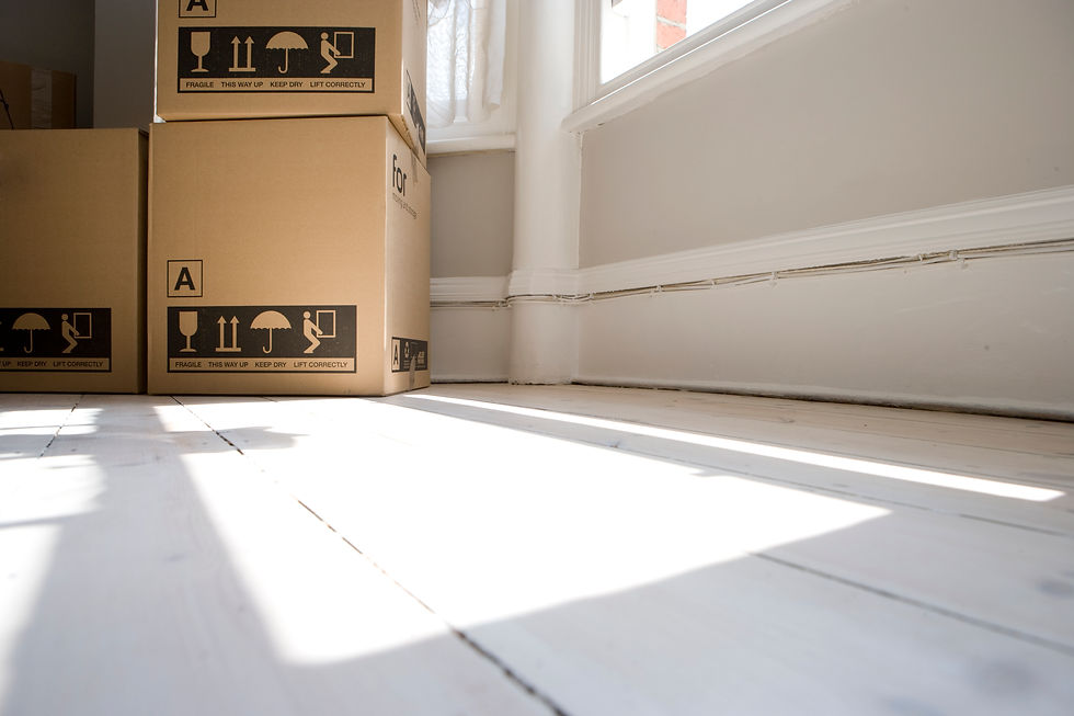 Low-angle shot of cardboard removal boxes stacked on sunlit wooden floor