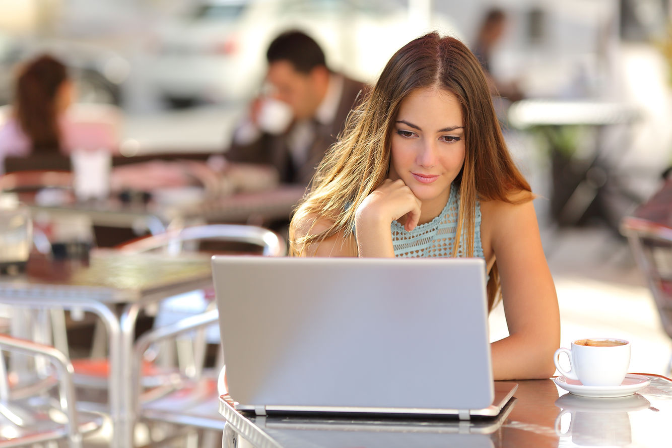 Attentive woman watching media in a laptop in a coffee shop with people in the background
