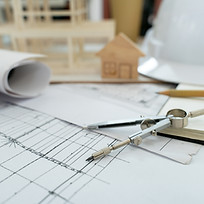 An architectural workspace with blueprints, a compass, and pencils on a desk