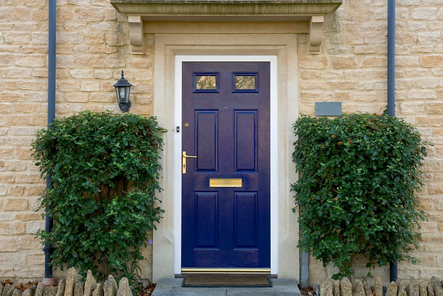 A classic blue door with a gold handle and mail slot is framed by stone walls