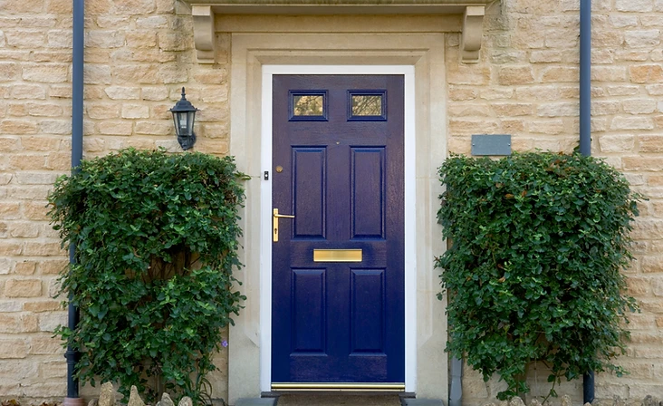 a classic dark blue paneled front door set within a stone masonry facade and flanked by trimmed green shrubs