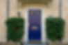Close-up of a navy blue front door with a gold letter plate on a beige stone facade