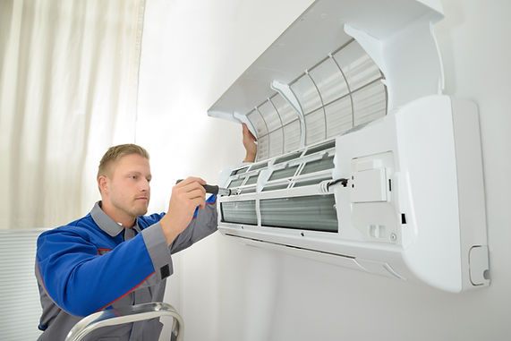 An HVAC technician uses a screwdriver to service an open indoor air conditioning unit