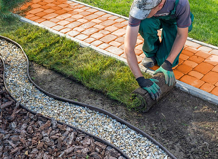 Professional landscaper in Auburn and Opelika, AL, laying fresh sod next to a decorative orange brick pathway, highlighting RIP Landscapes' premium landscaping services