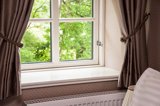 Interior view of a white multi-pane window with dark tied-back curtains looking out onto lush green foliage
