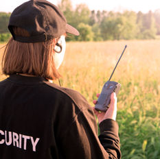 a women holding a walkie talkie while standing in a field, appearing as a security guard