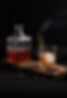 Black background, Rectangular glass alcohol decanter with a glass of whiskey with ice and rosemare on a wooden board