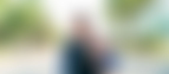 A woman in a hijab runs on a sunny urban street. Trees line the road, and people walk in the background. She looks determined.