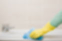 A person in yellow rubber gloves wipes down a bathtub with a blue cleaning cloth
