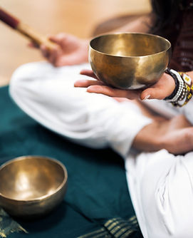 A sound bowl healing session with a person sitting on the floor holding the tibetian sound bowls