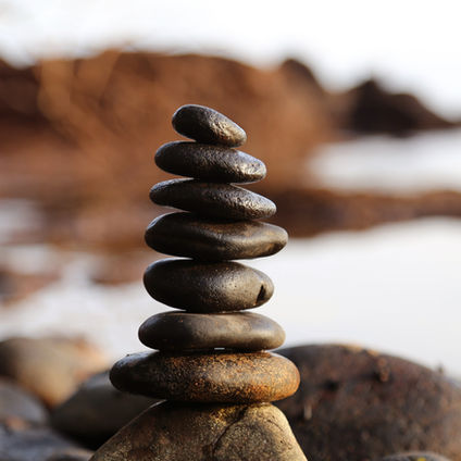 Stack of smooth black stones balanced on a shore, with a blurred water background. Calm and serene atmosphere.
