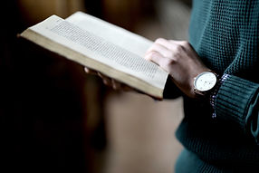 A book open on pages and held by a hand with a watch on the wrist