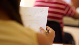 Person holding an "Intermediate Test" paper with an A+ grade. Background shows a red and white striped shirt, creating a positive mood.