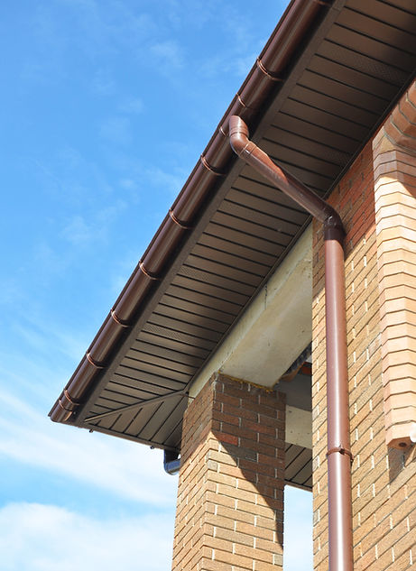 Close-up of a brick building's roof edge with a brown gutter and downspout against a clear blue sky