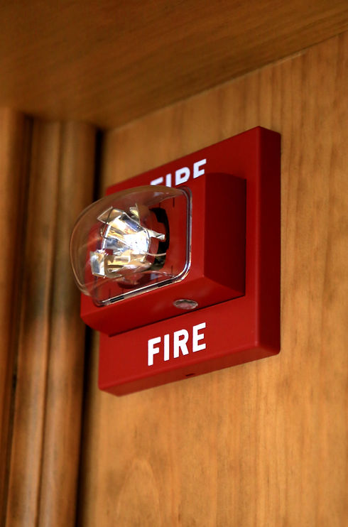 Red fire alarm strobe unit mounted on a wood-panelled wall