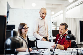 Smiling business professional pointing at data on a whiteboard during a team meeting