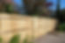 A long wooden slat fence casting shadows in the sunlight