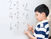 Boy in striped shirt solves math on whiteboard, counting on fingers. Equations include "2+2=4" and "4+2=6". Focused expression.