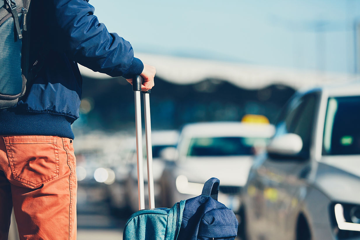 A man holding a suitcase, with a car visible behind him