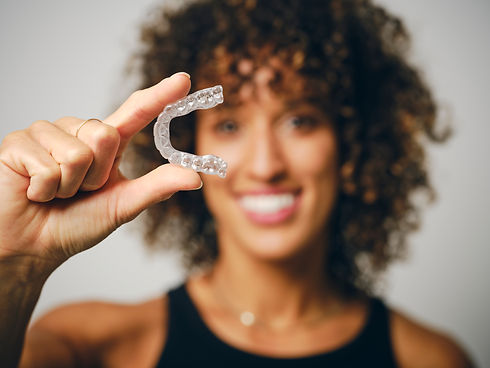 A smiling woman holding an invisible teeth aligner