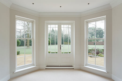 Bright interior room with white double doors and surrounding windows opening onto a garden