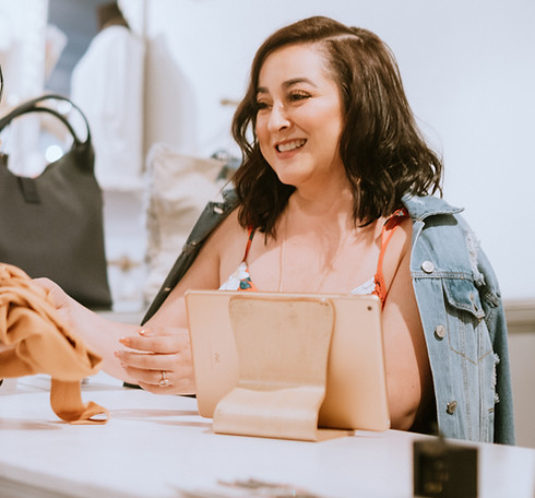 Clothing store business owners smiles while taking item from customer at the cash register.