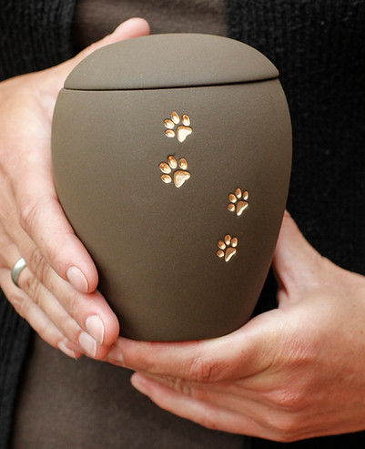 Woman holding brown ceramic pet urn with golden paw prints across the side